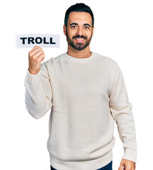 Young hispanic man with beard holding troll banner looking positive and happy standing and smiling with a confident smile showing teeth