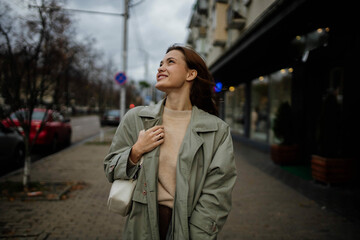 Fototapeta premium beautiful cheerful woman walks around the city in a gray coat in the spring near the shops