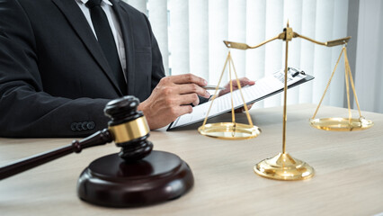 A male lawyer or notary working with contract papers, book and wooden gavel on table in courtroom, Law and Legal services concept