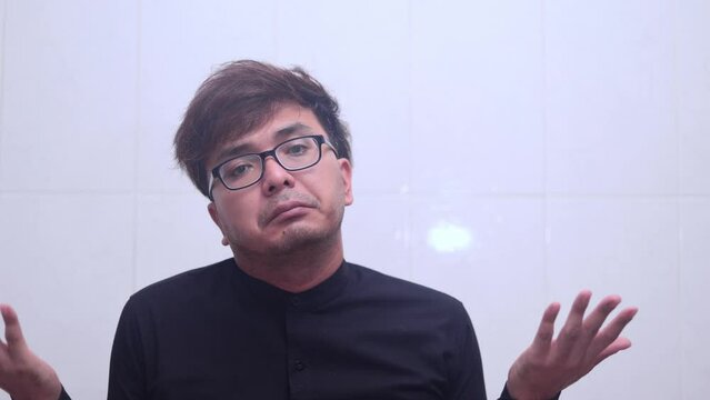 Asian man shrugging shoulder looking at camera.