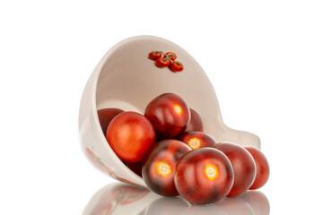 Several ripe black cocktail tomatoes with white ceramic cup, macro, isolated on white background.