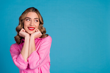 Photo of lovely young lady dreamy fists touch cheeks look empty space dressed stylish pink garment hairdo isolated on blue color background