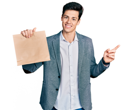 Young hispanic business man holding paper bag with bread smiling happy pointing with hand and finger to the side