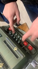 Fingers typing on a very old calculator machine.