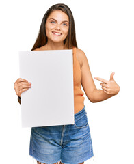 Young caucasian woman holding blank empty banner smiling happy pointing with hand and finger