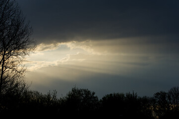 Sun rays against the background of gray rain clouds at sunset.