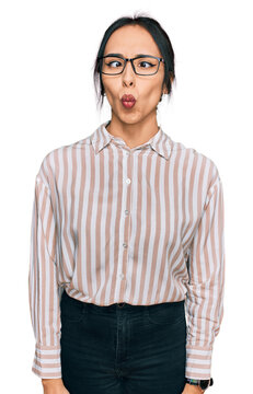 Young hispanic girl wearing casual clothes and glasses making fish face with lips, crazy and comical gesture. funny expression.