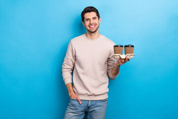 Photo of satisfied good mood pleasant guy dressed white pullover arms in pocket hold two takeaway cups isolated on blue color background - obrazy, fototapety, plakaty