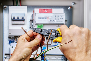 An electrician uses stripper cutter tool to remove insulation from ends of wires when connecting...