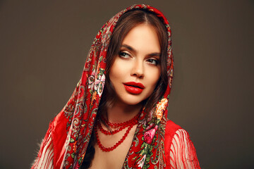 Russian girl Matryoshka style. Fashion woman portrait with traditional red headscarf. Beauty girl model with red lips makeup isolated on studio background. - 775209985