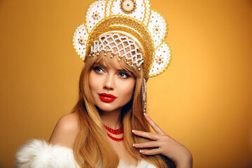 Beautiful blonde woman portrait in fur coat and kokoshnik (woman's headdress in old Russia). Pretty model girl with red lips and plait hairstyle isolated on grey studio background.