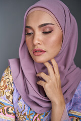 Beautiful female model wearing modern batik kebaya, sitting on a chair isolated over grey background. Eidul fitri festival fashion and beauty concept.