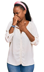 Young black woman wearing casual clothes smelling something stinky and disgusting, intolerable smell, holding breath with fingers on nose. bad smell