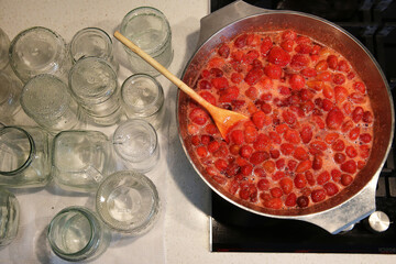 Cooking strawberry jam in a large bowl at home. Wooden spoon in a bowl with jam. Empty glass jars for jam.