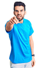 Young handsome man with beard wearing casual t-shirt pointing displeased and frustrated to the camera, angry and furious with you