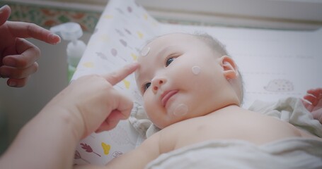 Portrait little cute asian newborn infant baby child looking at camera while mother applying...