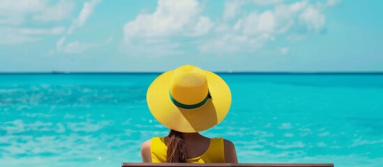 Woman in yellow hat sitting on bench looking at ocean