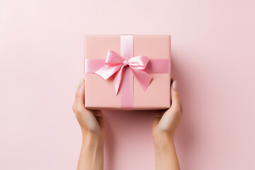 Minimal pink background with woman hands holding a wrapped gift box seen from above for a birthday 