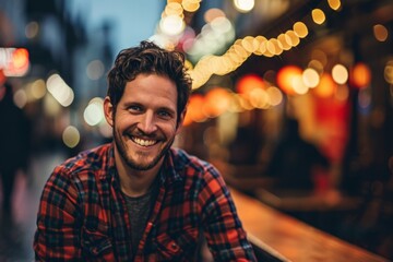 Portrait of a handsome young man in a plaid shirt smiling at the camera. - obrazy, fototapety, plakaty