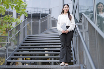 Professional woman in a white shirt poses confidently by the stairs