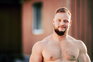 Pleasant young athletic shirtless European man with goatee on outdoors near rural house.