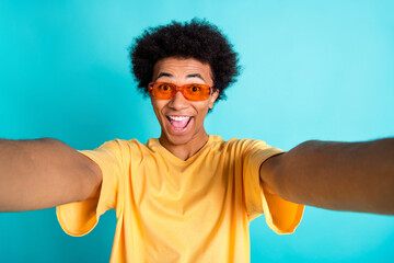 Photo of overjoyed funky guy with afro hair dressed yellow t-shirt in sunglass making selfie...