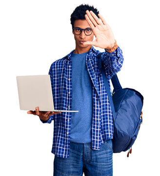 Young african american man holding student backpack using laptop with open hand doing stop sign with serious and confident expression, defense gesture