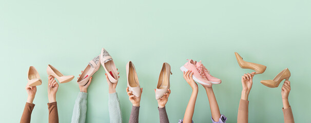 Many hands with different stylish shoes on color background