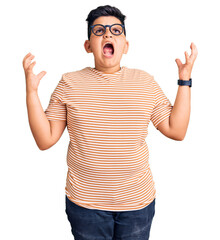 Naklejka premium Little boy kid wearing casual clothes and glasses crazy and mad shouting and yelling with aggressive expression and arms raised. frustration concept.