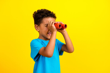 Portrait of funny schoolboy with afro hair wear blue stylish t-shirt look in binoculars at empty...