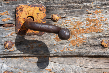 Close-up of old rusty iron handle door on weather-damaged antique wooden door