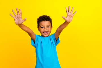 Portrait of beautiful small preteen schoolboy with afro hair wear blue t-shirt raising hands count to ten isolated on yellow background
