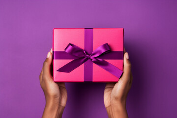 Minimal purple or magenta background with male hands holding a wrapped gift box seen from above for a birthday  - obrazy, fototapety, plakaty