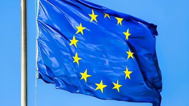 Flag of Europe blue color with yellow stars waving in the wind on blue sky.