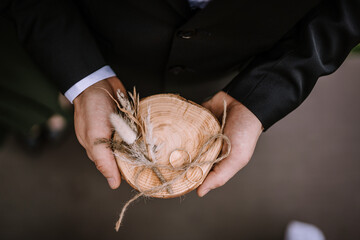 Valmiera, Latvia - Augist 13, 2023 - Hands holding a wooden bowl with two wedding rings and...