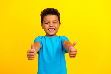 Portrait of optimistic nice schoolboy with afro hair wear blue t-shirt showing thumbs up good work isolated on vivid yellow background