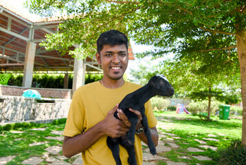 Indian man Cradles Young Black Goat on Sunny Farm