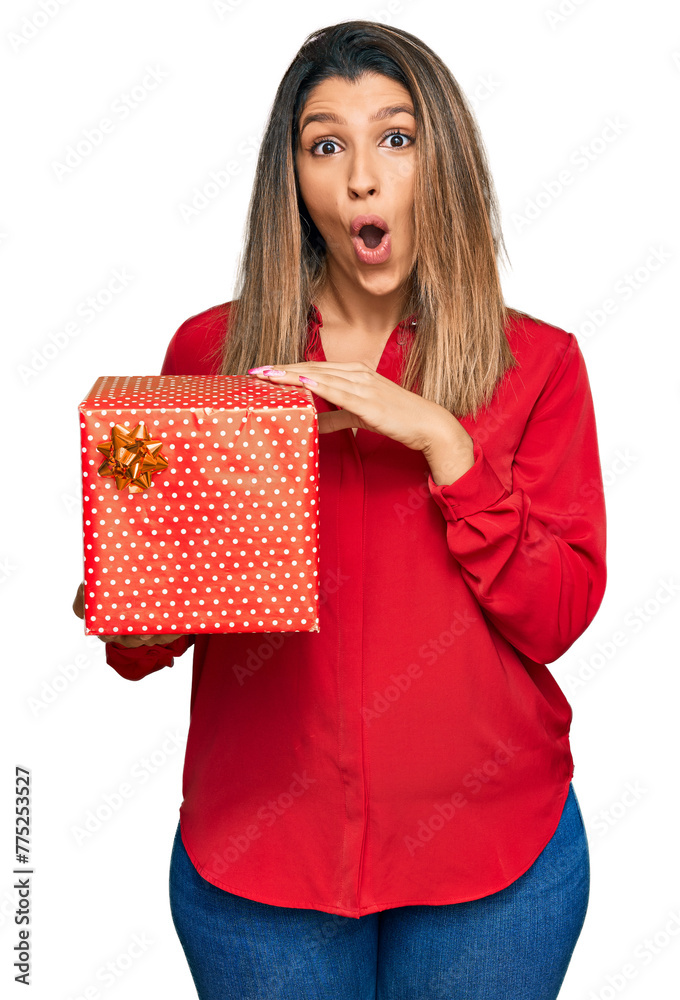 Sticker beautiful brunette woman holding gift scared and amazed with open mouth for surprise, disbelief face