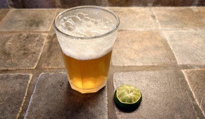 glass of Mexican beer and squeezed lime on a porcelain tiled countertop - 775254964