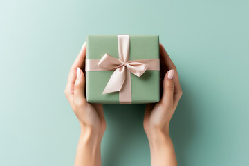 Minimal green background with woman hands holding a wrapped gift box seen from above for a birthday 