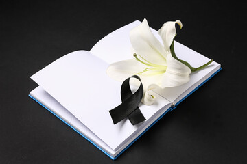 Beautiful lily flower with blank book and black funeral ribbon on dark background