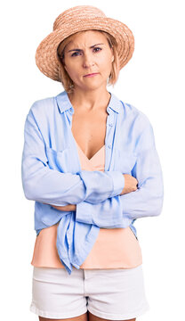 Young blonde woman wearing summer hat skeptic and nervous, disapproving expression on face with crossed arms. negative person.