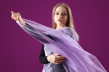 Beautiful young woman in bodysuit with fabric on purple background