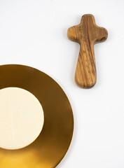Wooden cross, paten with altar bread, white background