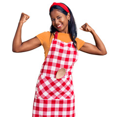 Young indian girl wearing professional baker apron showing arms muscles smiling proud. fitness...