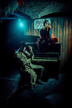 Detective in the raincoat and hat playing piano. Woman is sitting on the piano looking at performer.