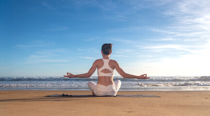 Outdoor yoga. Woman meditating, sitting in lotus position on fitness mat on beach, practicing meditation near ocean, back view