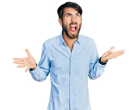 Hispanic man with blue eyes wearing business shirt crazy and mad shouting and yelling with aggressive expression and arms raised. frustration concept.