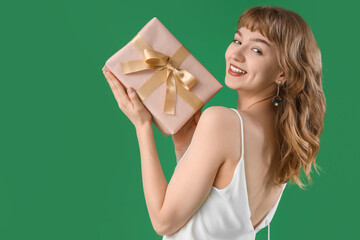 Beautiful young woman with gift box on green background
