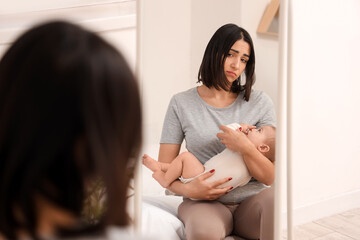 Young woman with her baby suffering from postnatal depression near mirror in bedroom